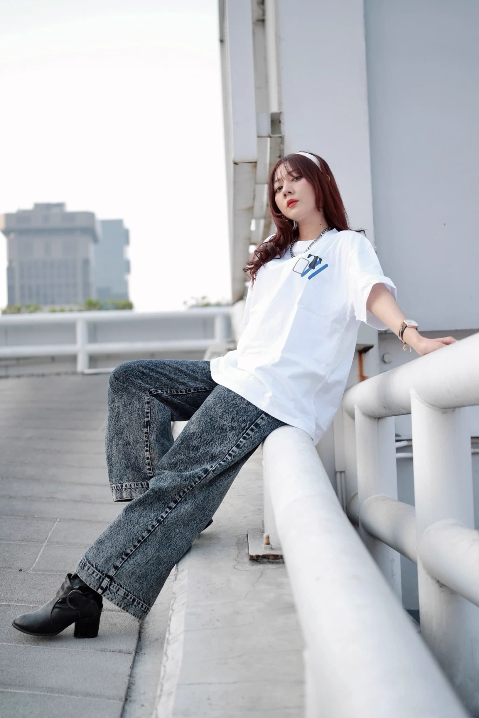 Woman seated on a rooftop railing in an oversized white T-shirt and wide-leg jeans