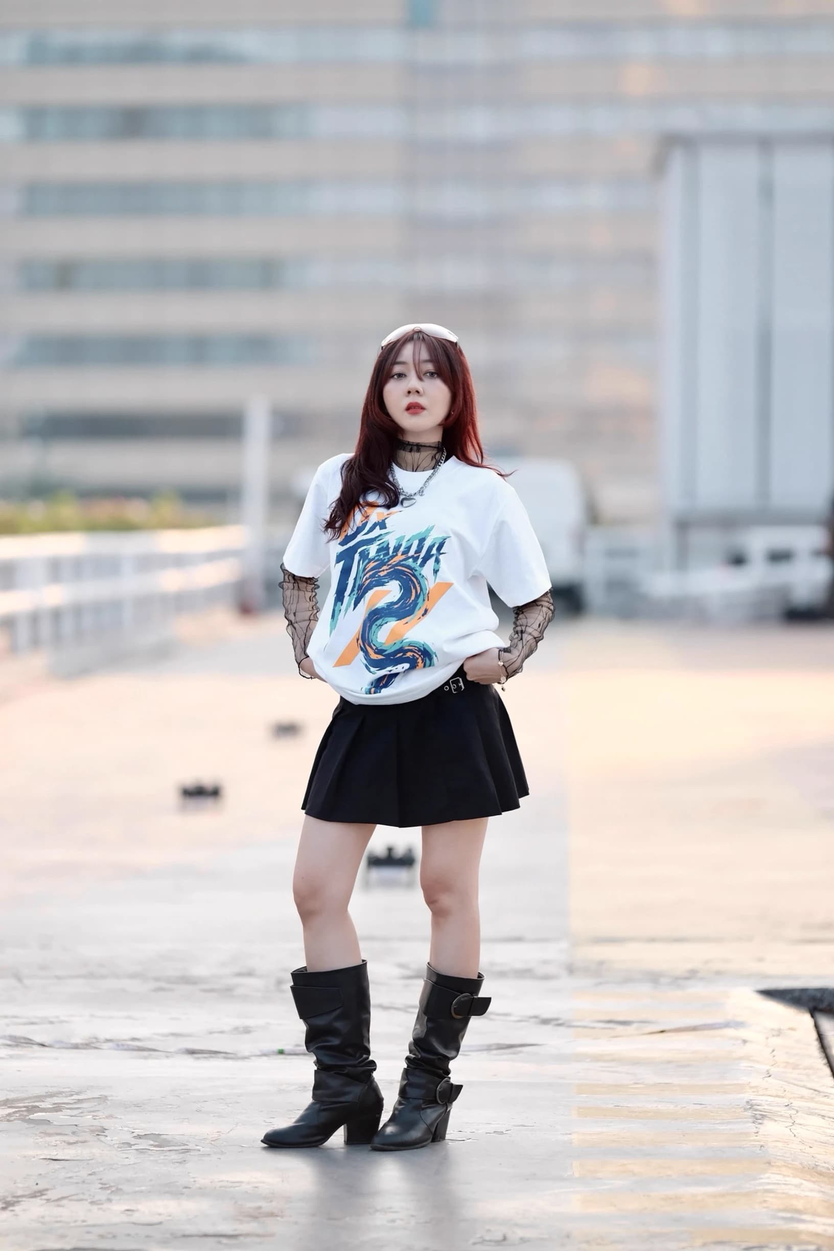Woman standing on a rooftop in a white graphic T-shirt, black skirt, and tall boots